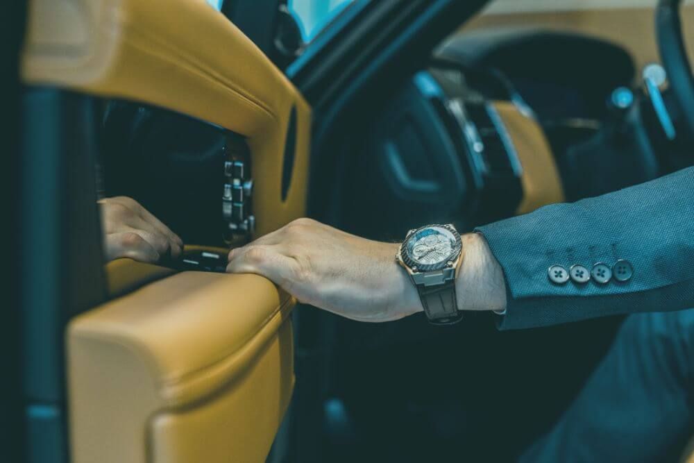 left hand with watch on it closing a leather interior car door